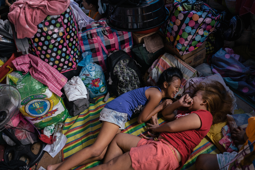 Dos jóvenes se ven en una cancha de baloncesto con sus pertenencias después de que un incendio tomara sus hogares en Manila, Filipinas.